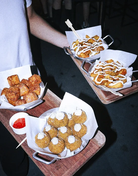 Garçom carregando bandejas com dadinhos de tapioca, batatas com molho e croquetas de cupim