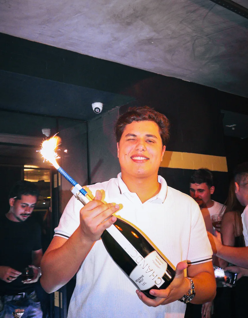 Rapaz comemorando com espumante e vela de fogos de artifício